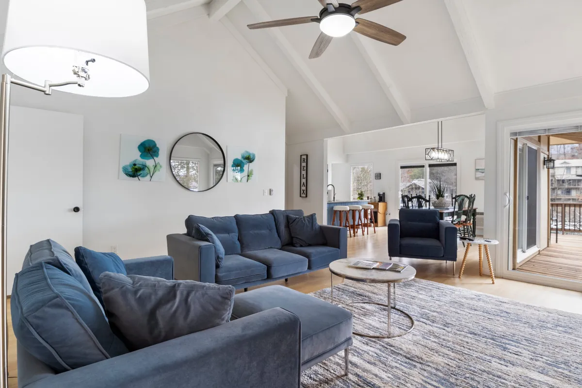 This scene showcases a comfortable living area with blue sofas, a round coffee table, stylish artwork, a large mirror, and the dining area visible in the background. The decor is modern yet welcoming, providing an inviting space for social gatherings or quiet moments.