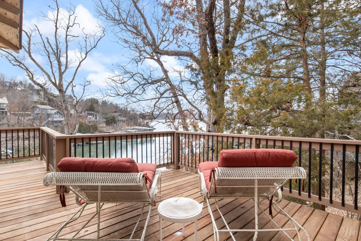 A welcoming wooden deck with red cushioned chairs overlooking the lake, offering inviting spaces for reading, relaxing, or enjoying a cup of coffee. The tranquil water view and cozy seating hint at evenings spent stargazing or sharing stories by the fireside.