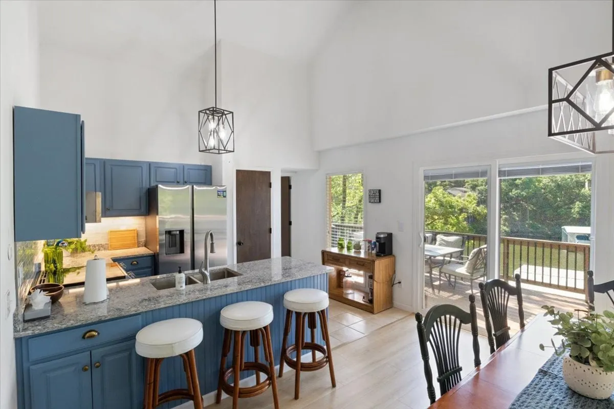 The photo showcases a contemporary kitchen island, surrounded by sleek stainless-steel appliances and a dining table set by large windows. The arrangement is inviting for meal prep, family meals, or relaxed coffee breaks, with abundant natural light enhancing the ambiance.