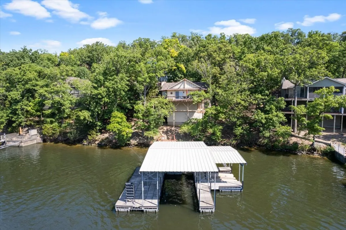 A tranquil lakeside setting featuring a private dock jutting out over the water, with the house and trees visible nearby. The scene is perfect for boating, fishing, picnicking, and swimming, and captures the essence of lakeside relaxation.