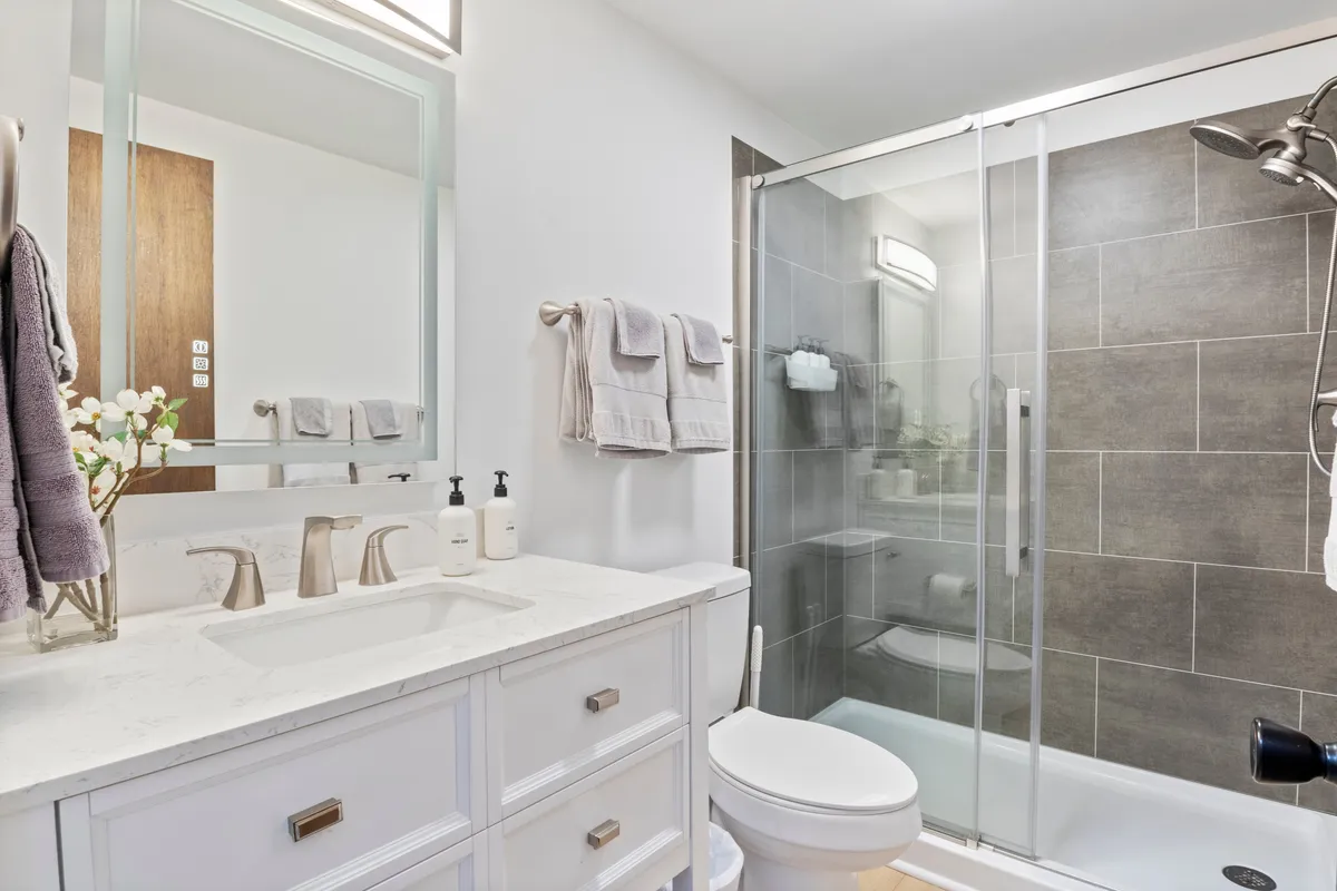 A spacious bathroom with a dual-sink vanity, glass shower enclosure, and plush decorative towels. The color palette is soft and inviting, with plenty of light and a spa-like ambiance.