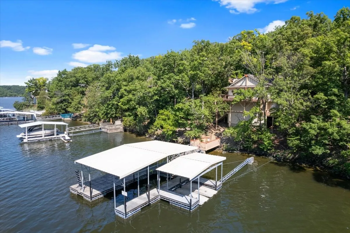 A peaceful lakeside view with a private dock stretching out over the water, surrounded by trees and with a house visible in the distance. The scene includes the dock, perfect for boating and fishing, and captures the serene atmosphere at sunset.