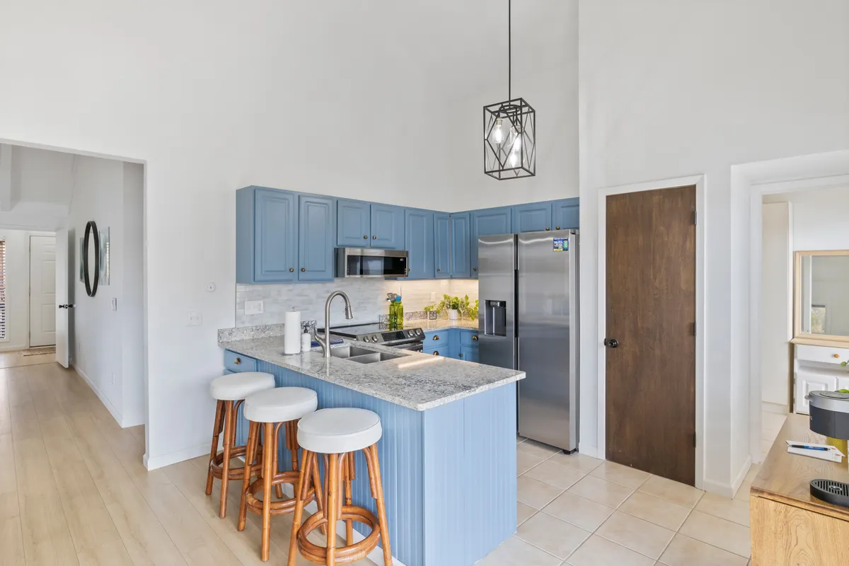 This image features a modern kitchen with blue cabinetry, a gleaming granite countertop, inviting bar stools, and stylish pendant lighting. The space is designed for both cooking and socializing, with ample counter space perfect for meal prep or serving snacks.