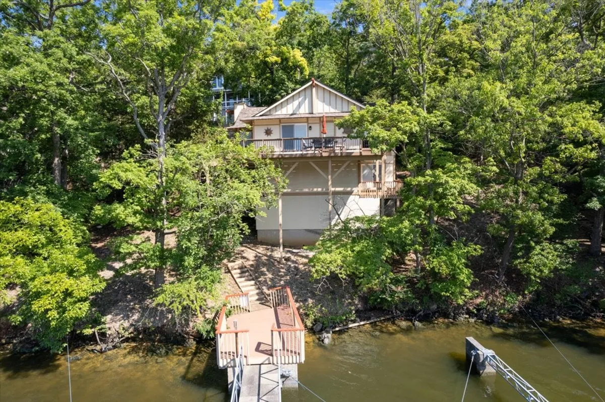 A wide exterior view capturing both the house and its private dock, framed by lush greenery. The image showcases the peaceful waters and the inviting outdoor spaces, suggesting easy access to lakeside relaxation and adventures.